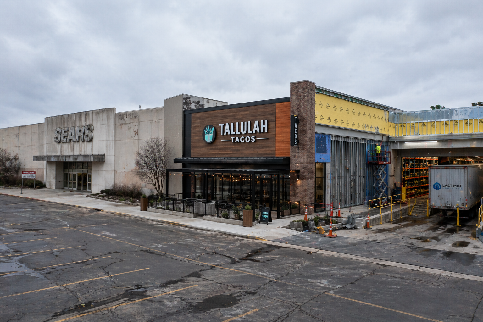 A former shopping mall being converted into a mixed-use development, with construction scaffolding on part of the structure, a new restaurant facade visible at ground level, and an industrial logistics bay added to the far end.